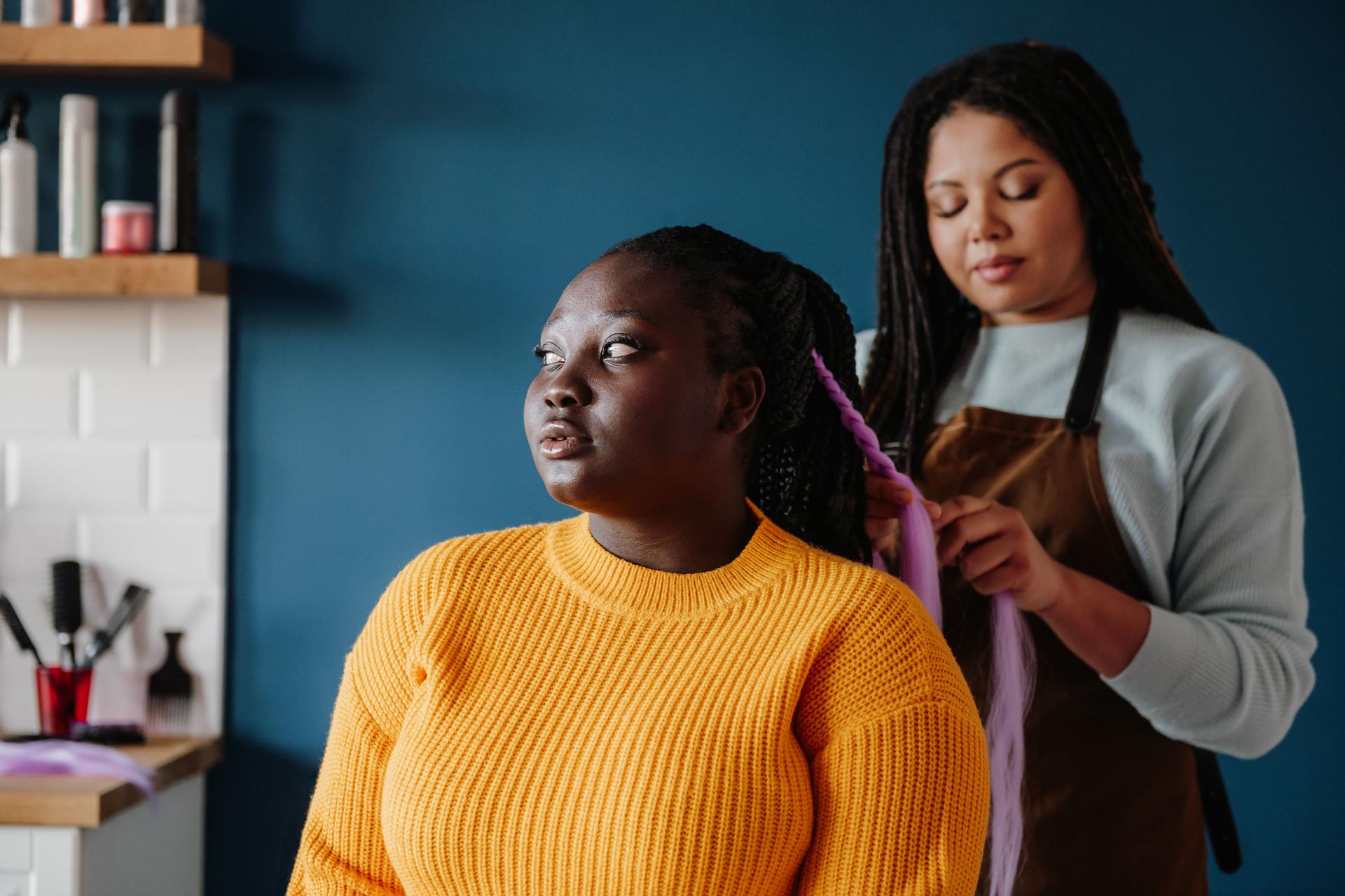 Confident African hairdresser braiding hair to female customer in salon